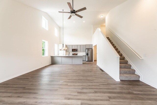 325 Woods Edge Loop, Pataskala, OH 43062 - unfurnished living room featuring a towering ceiling, a ceiling fan, stairway, wood finished floors, and baseboards