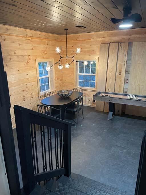 dining area featuring a ceiling fan, wood ceiling, concrete flooring, and wooden walls