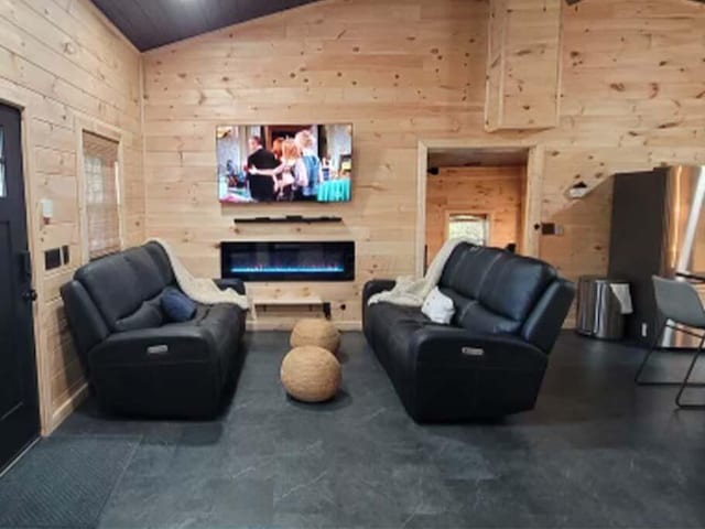 living room featuring wood walls, wood ceiling, a glass covered fireplace, and high vaulted ceiling