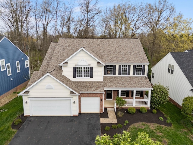traditional home with roof with shingles, driveway, covered porch, brick siding, and an attached garage