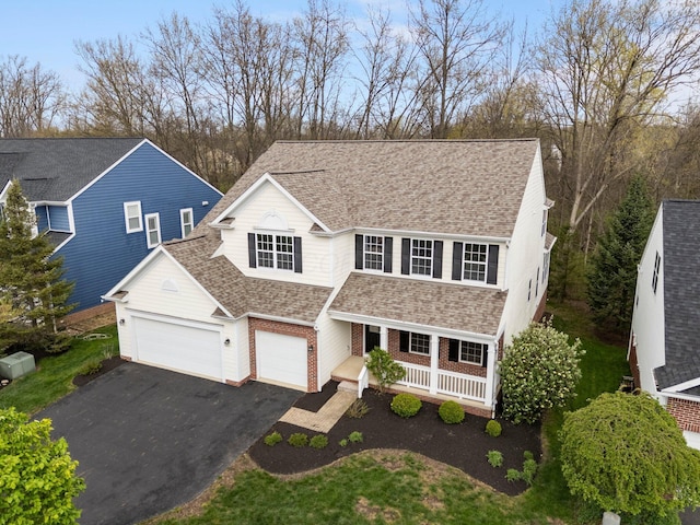 traditional home featuring aphalt driveway, an attached garage, a porch, brick siding, and roof with shingles
