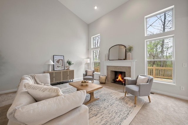 living area featuring baseboards, high vaulted ceiling, a lit fireplace, and light colored carpet