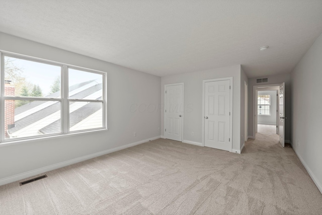 unfurnished bedroom featuring baseboards, visible vents, and light colored carpet