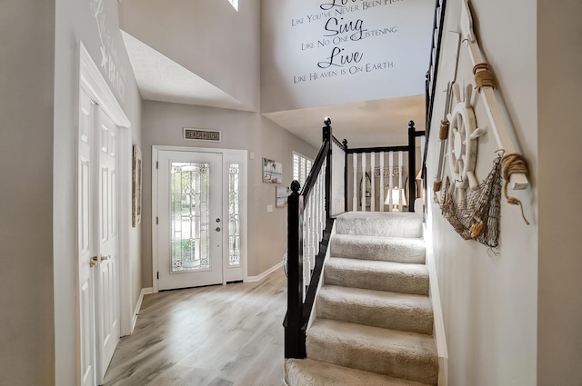 foyer featuring baseboards, wood finished floors, a high ceiling, and stairway