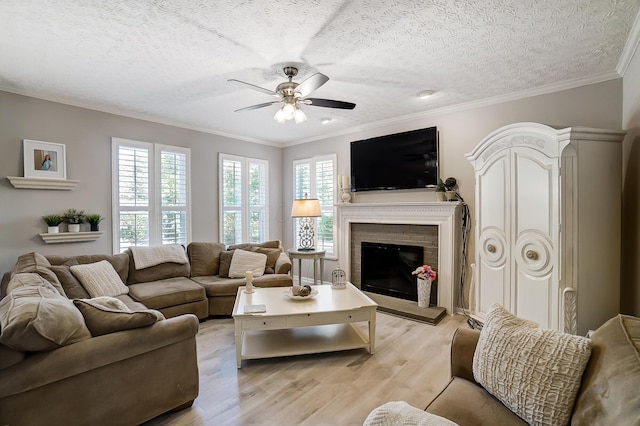 living room featuring light wood finished floors, a brick fireplace, a textured ceiling, and ceiling fan