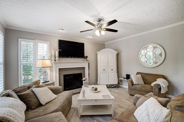 living area featuring ornamental molding, light wood-style floors, a fireplace, a textured ceiling, and ceiling fan