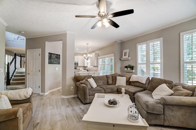 living room featuring light wood-style flooring, baseboards, ceiling fan with notable chandelier, stairway, and crown molding