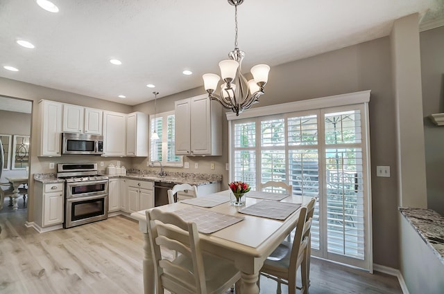 kitchen featuring light stone counters, a sink, light wood-style floors, appliances with stainless steel finishes, and a notable chandelier