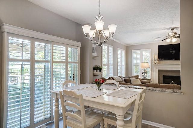 dining space featuring a textured ceiling, a brick fireplace, ornamental molding, and ceiling fan with notable chandelier