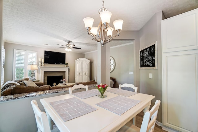 dining room featuring a fireplace, ornamental molding, a textured ceiling, and ceiling fan with notable chandelier