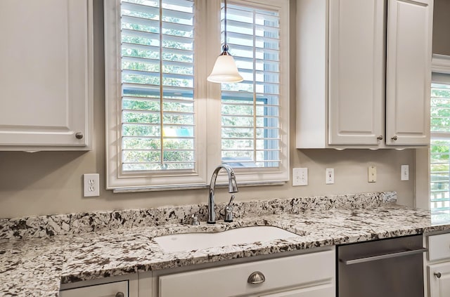 kitchen featuring white cabinets, light stone countertops, stainless steel dishwasher, and a sink