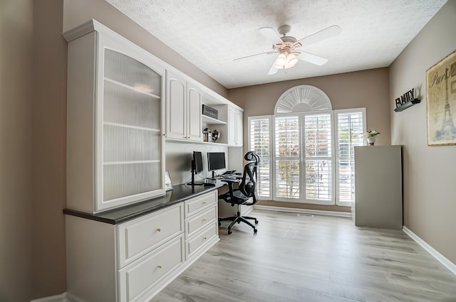 office featuring ceiling fan, baseboards, light wood-style floors, and a textured ceiling