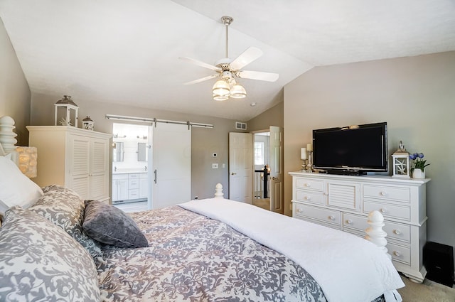 bedroom featuring a barn door, vaulted ceiling, connected bathroom, light carpet, and visible vents