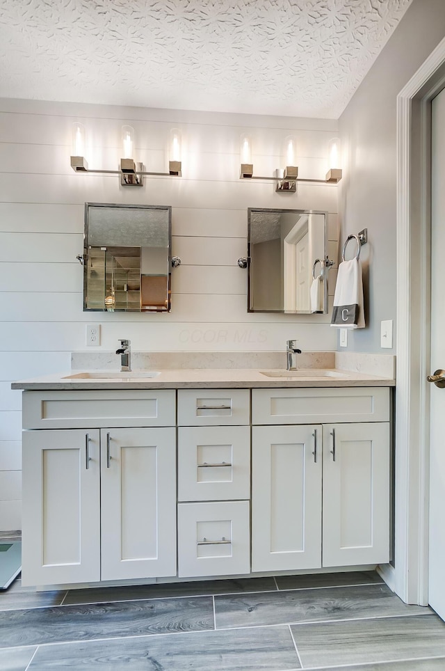 bathroom featuring double vanity, wood finished floors, a textured ceiling, and a sink