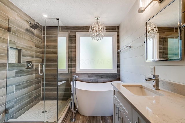 bathroom with a freestanding bath, a notable chandelier, wood finished floors, a shower stall, and vanity