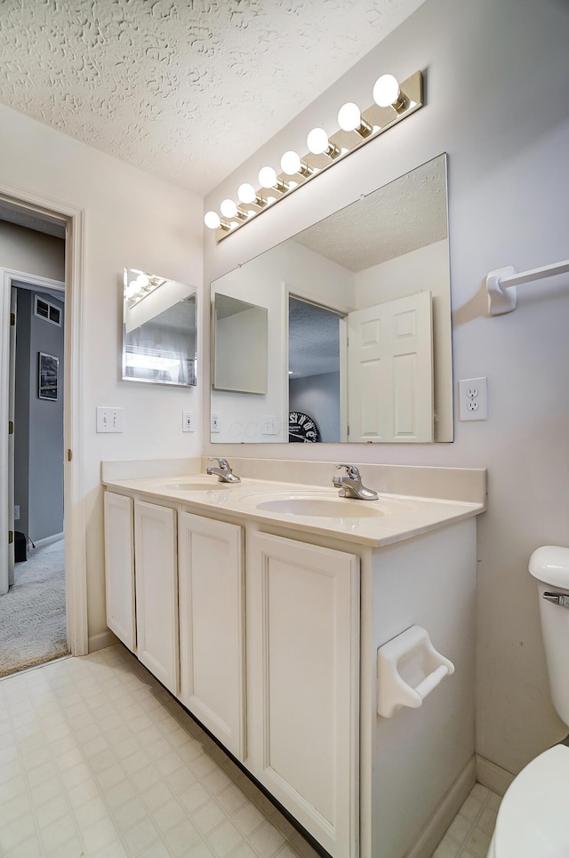 bathroom with toilet, a sink, and double vanity