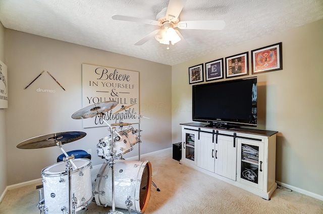 recreation room with light carpet, a ceiling fan, a textured ceiling, and baseboards