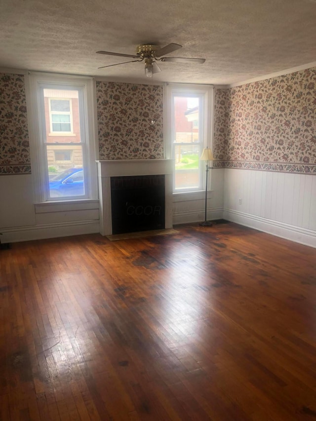 unfurnished living room featuring a wainscoted wall, wallpapered walls, wood finished floors, and a fireplace with flush hearth