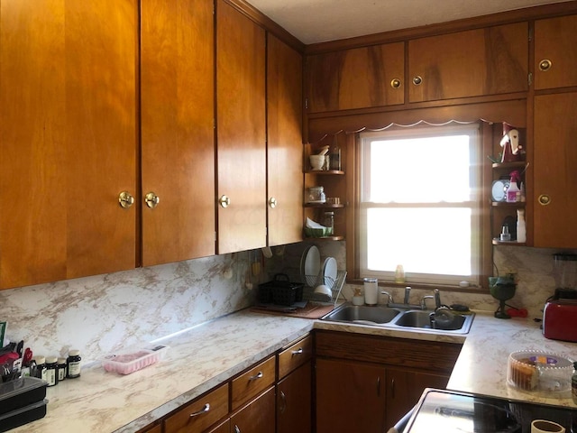 kitchen with decorative backsplash, brown cabinetry, open shelves, light countertops, and a sink