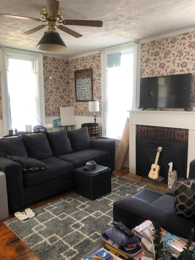 living room with a textured ceiling, wallpapered walls, a fireplace, wood finished floors, and a ceiling fan