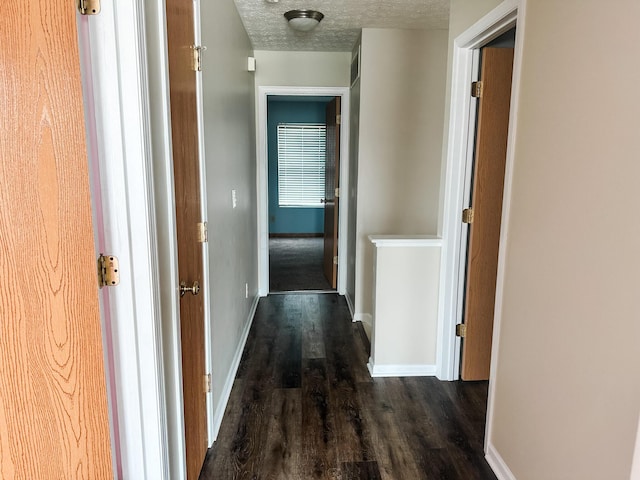 hall featuring a textured ceiling, dark wood finished floors, and baseboards