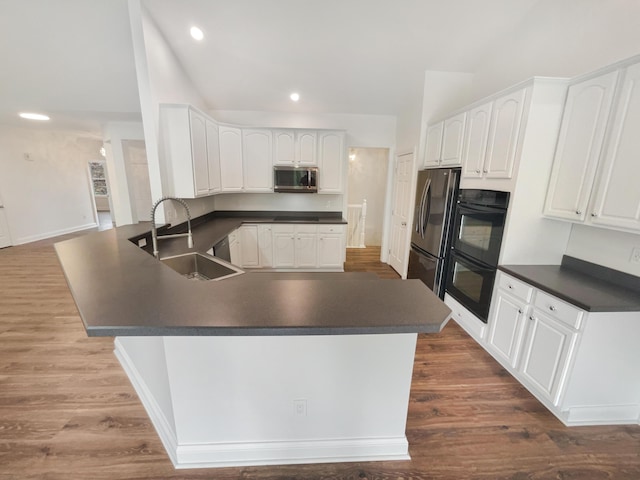 kitchen featuring dark countertops, a sink, dark wood finished floors, a peninsula, and appliances with stainless steel finishes
