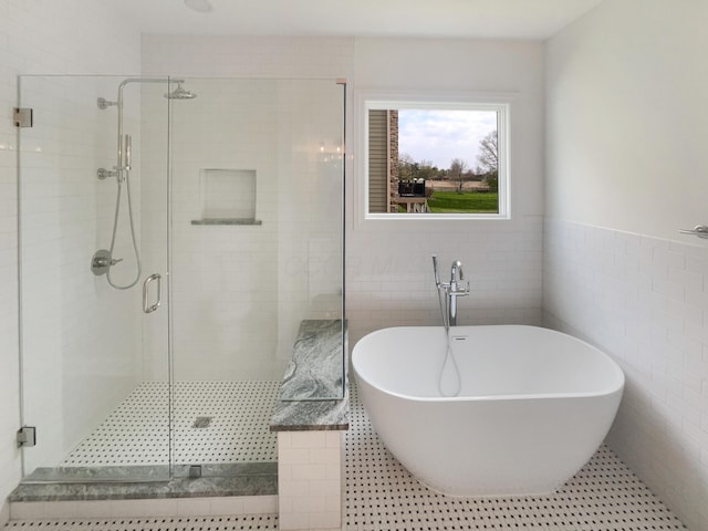 bathroom featuring tile patterned floors, tile walls, wainscoting, a soaking tub, and a stall shower