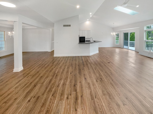 unfurnished living room with a chandelier, lofted ceiling with skylight, visible vents, and a sink