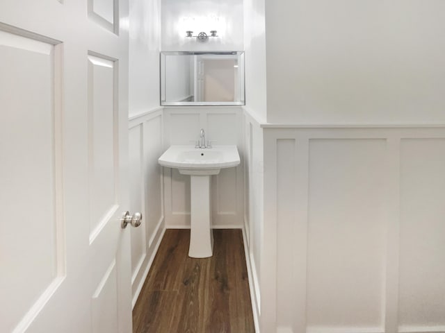 bathroom with wainscoting, wood finished floors, and a decorative wall