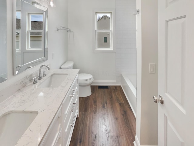bathroom with wood finished floors, a sink, double vanity, toilet, and visible vents