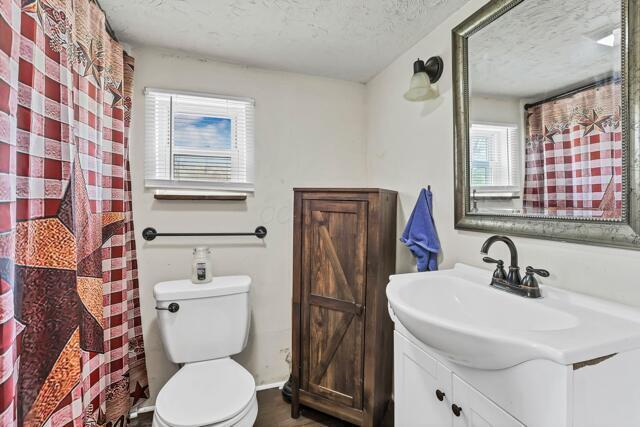 full bath featuring a textured ceiling, vanity, curtained shower, baseboards, and toilet