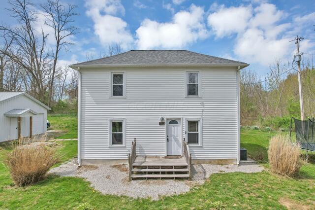 back of property with central AC unit, a trampoline, an outdoor structure, a lawn, and a deck