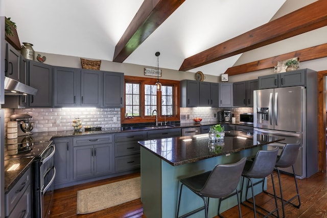 kitchen featuring lofted ceiling with beams, a sink, decorative backsplash, under cabinet range hood, and appliances with stainless steel finishes