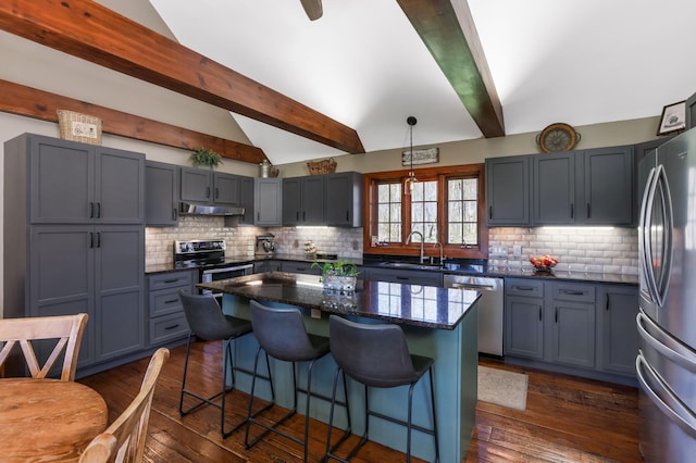 kitchen with dark wood finished floors, under cabinet range hood, vaulted ceiling with beams, a sink, and appliances with stainless steel finishes