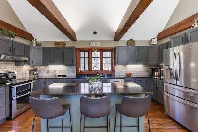 kitchen featuring a breakfast bar, under cabinet range hood, stainless steel appliances, and vaulted ceiling with beams