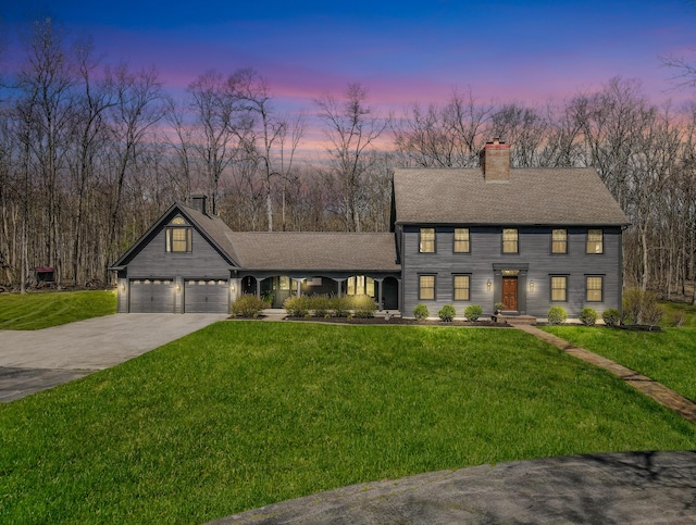 colonial home featuring a chimney, a yard, an attached garage, driveway, and roof with shingles