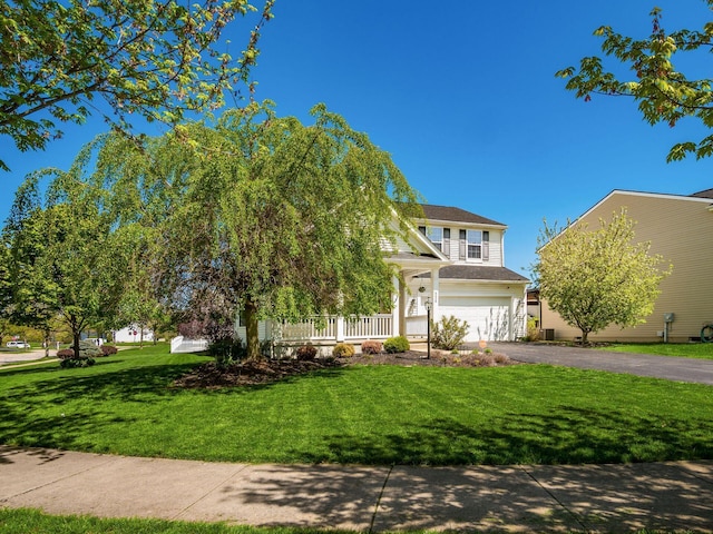 view of property hidden behind natural elements featuring an attached garage, a porch, a front lawn, and aphalt driveway