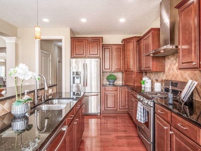 7766 Dickens Ct, Delaware, OH 43015 - kitchen featuring stainless steel appliances, a sink, dark stone counters, wall chimney range hood, and hanging light fixtures