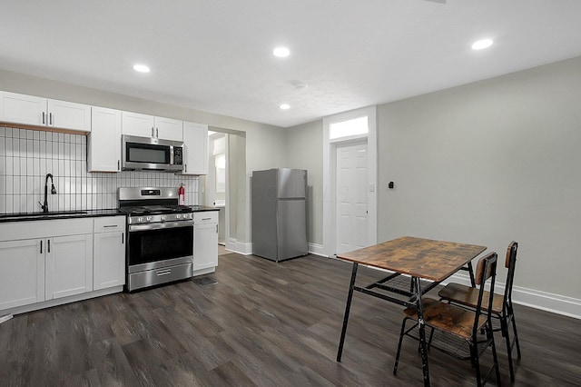 kitchen featuring dark countertops, a sink, baseboards, appliances with stainless steel finishes, and dark wood-style floors