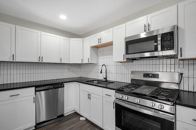 kitchen with dark countertops, a sink, stainless steel appliances, backsplash, and white cabinetry