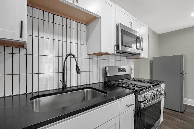 kitchen with dark countertops, a sink, white cabinets, stainless steel appliances, and backsplash