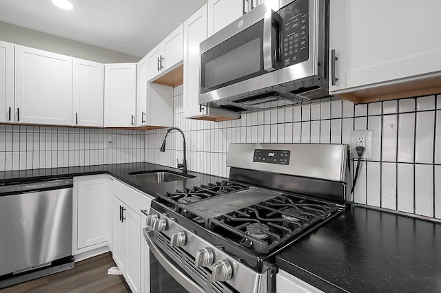 kitchen with stainless steel appliances, backsplash, dark countertops, a sink, and white cabinetry