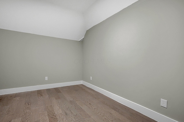 spare room featuring baseboards, dark wood-style flooring, and vaulted ceiling