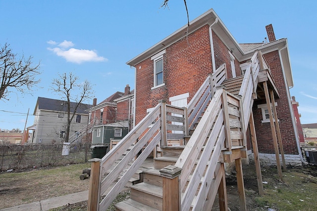 rear view of house with stairway, a chimney, central AC unit, fence, and brick siding