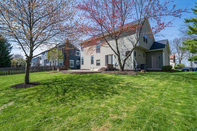 rear view of house featuring fence, a lawn, entry steps, and central AC
