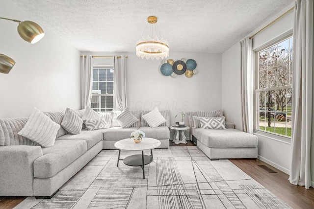 living area featuring a wealth of natural light, a chandelier, wood finished floors, and visible vents