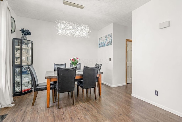 dining space with wood finished floors, a textured ceiling, baseboards, and an inviting chandelier