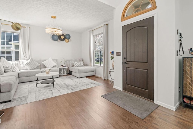 entryway featuring baseboards, wood finished floors, a textured ceiling, and a notable chandelier