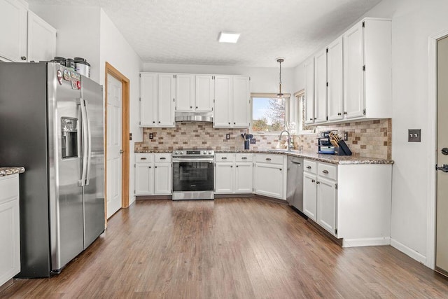 kitchen featuring light stone counters, under cabinet range hood, stainless steel appliances, and white cabinetry