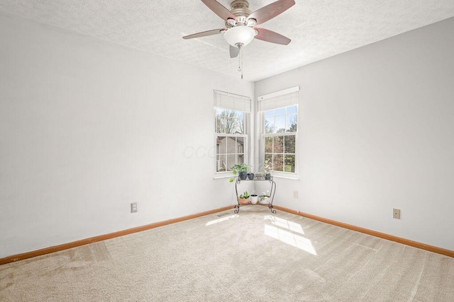 carpeted empty room featuring a textured ceiling, a ceiling fan, and baseboards